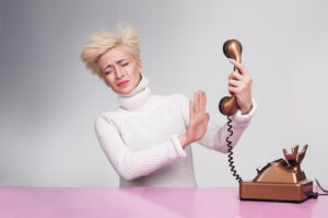 Woman holding phone away from her face and trying to block the speaker with her hand to block verbal abuse