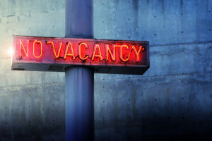 Glowing retro neon 'no vacancy' sign against cool blue wall background